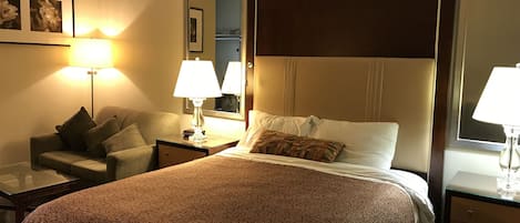 A hotel room with a large bed, a sofa, a desk, and a mirror.