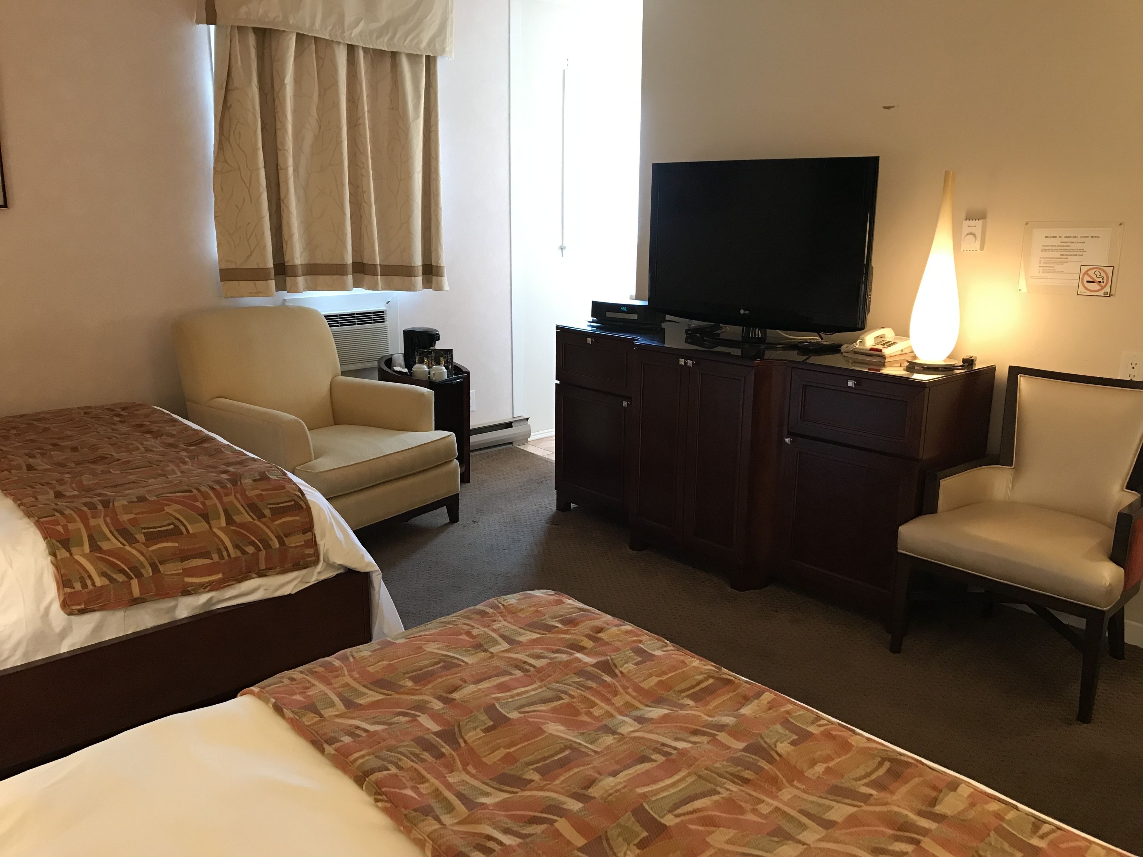 Une chambre d’hôtel avec deux lits, un bureau doté d’un téléviseur à écran plat, une chaise, une lampe et un placard.