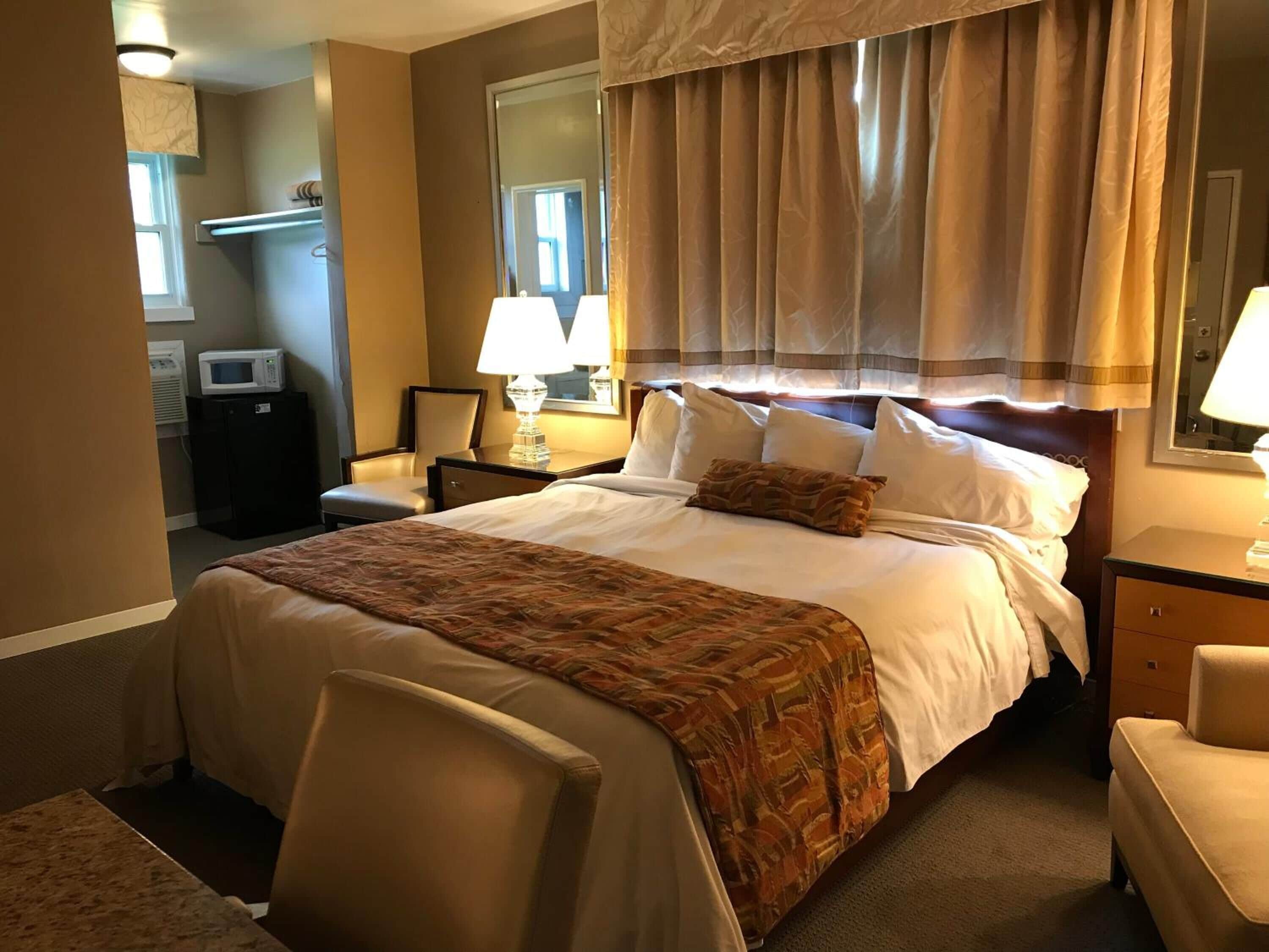 A hotel room with a large bed, a desk, a chair, a microwave, and a window with curtains.