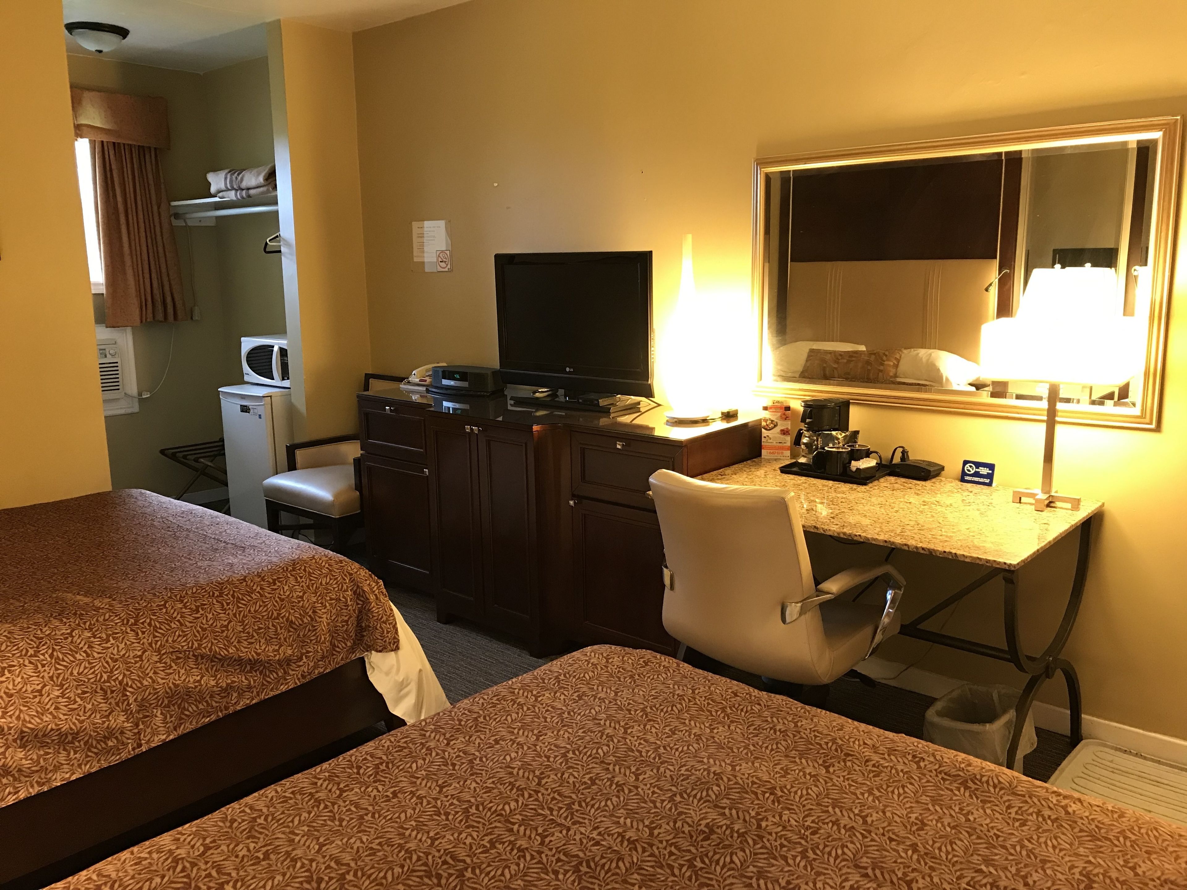 A hotel room with two beds, a desk with a computer, a TV, and a lamp.