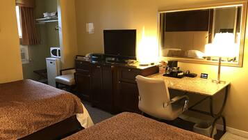A hotel room with two beds, a desk with a computer, a TV, and a lamp.