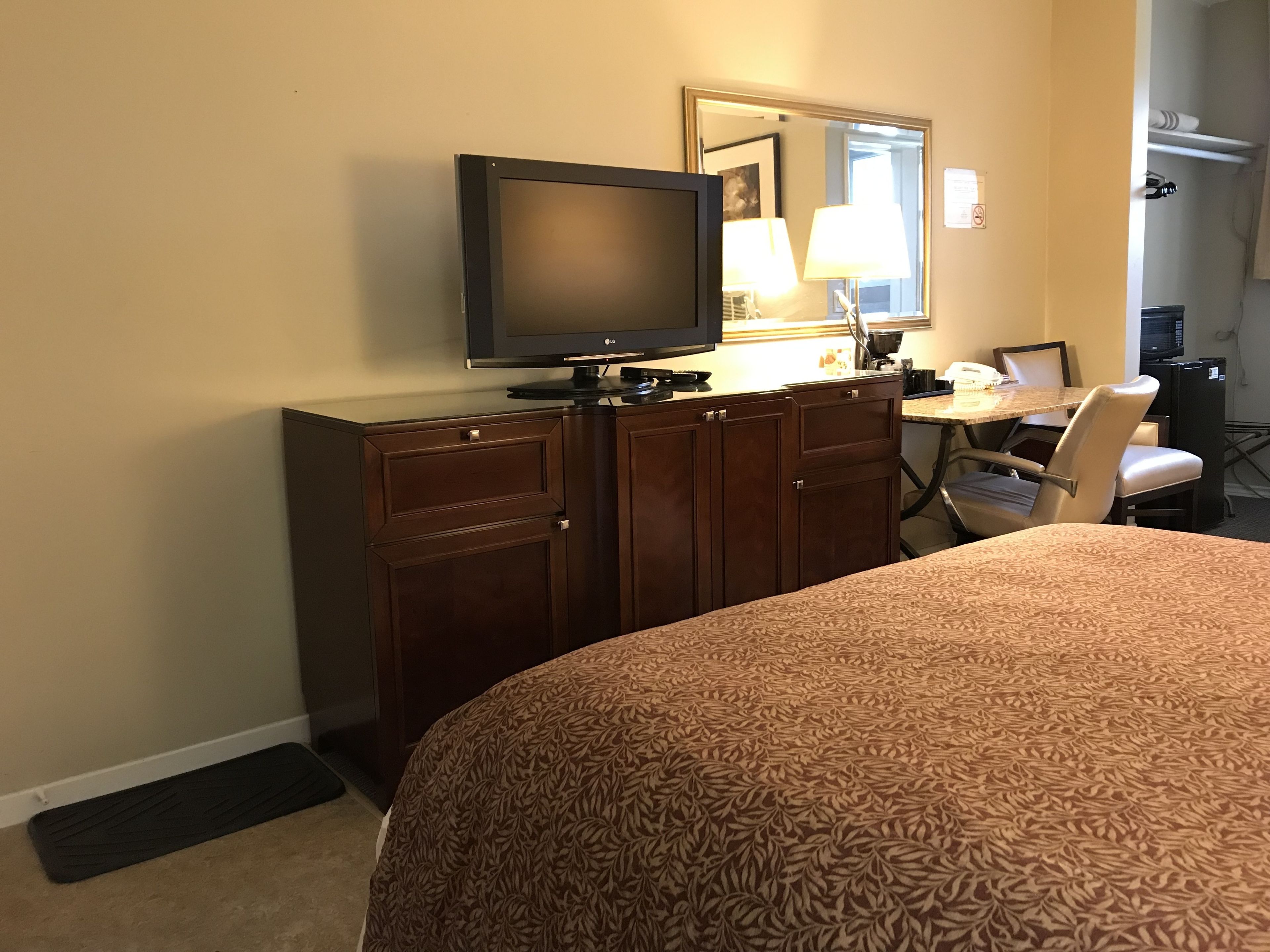 Una camera d'albergo con un letto, una scrivania, una sedia, una televisione e un armadio.