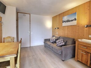 Un salon chaleureux avec un mur en bois, un canapé gris agrémenté de coussins à carreaux, une table à manger en bois et un buffet en bois.