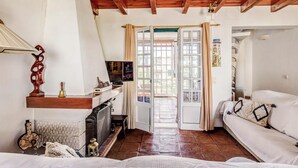A cozy living room with a fireplace, wooden ceiling beams, and a sliding glass door leading to an outdoor area.