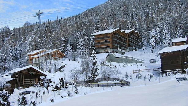 Un complejo turístico en la montaña cubierto de nieve, con edificios de madera y un telesilla.