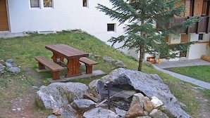 Un hogar de piedra con parrilla, una mesa de picnic y un pequeño árbol en un patio.