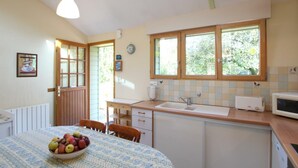 Eine Küche mit Esstisch, Obstschale, einer Uhr und einem Fenster mit Blick auf Grünflächen.