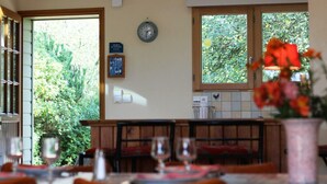 Ein Essbereich mit Blick auf Grün durch das Fenster, eine Uhr an der Wand und ein Schild, das auf ein touristisch orientiertes Lokal hinweist.