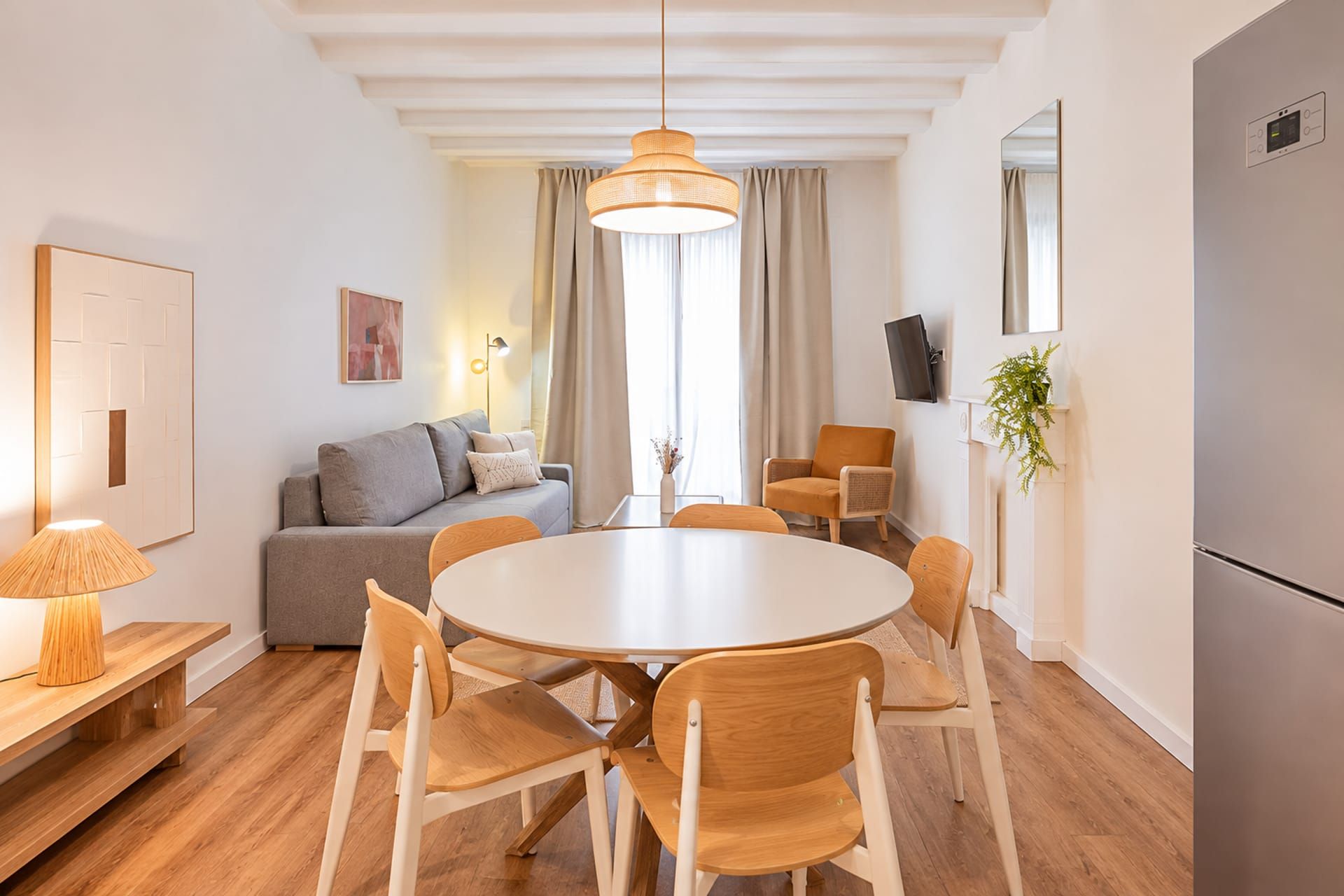 A modern kitchen with a round dining table, wooden chairs, a sofa, and a hanging light fixture.