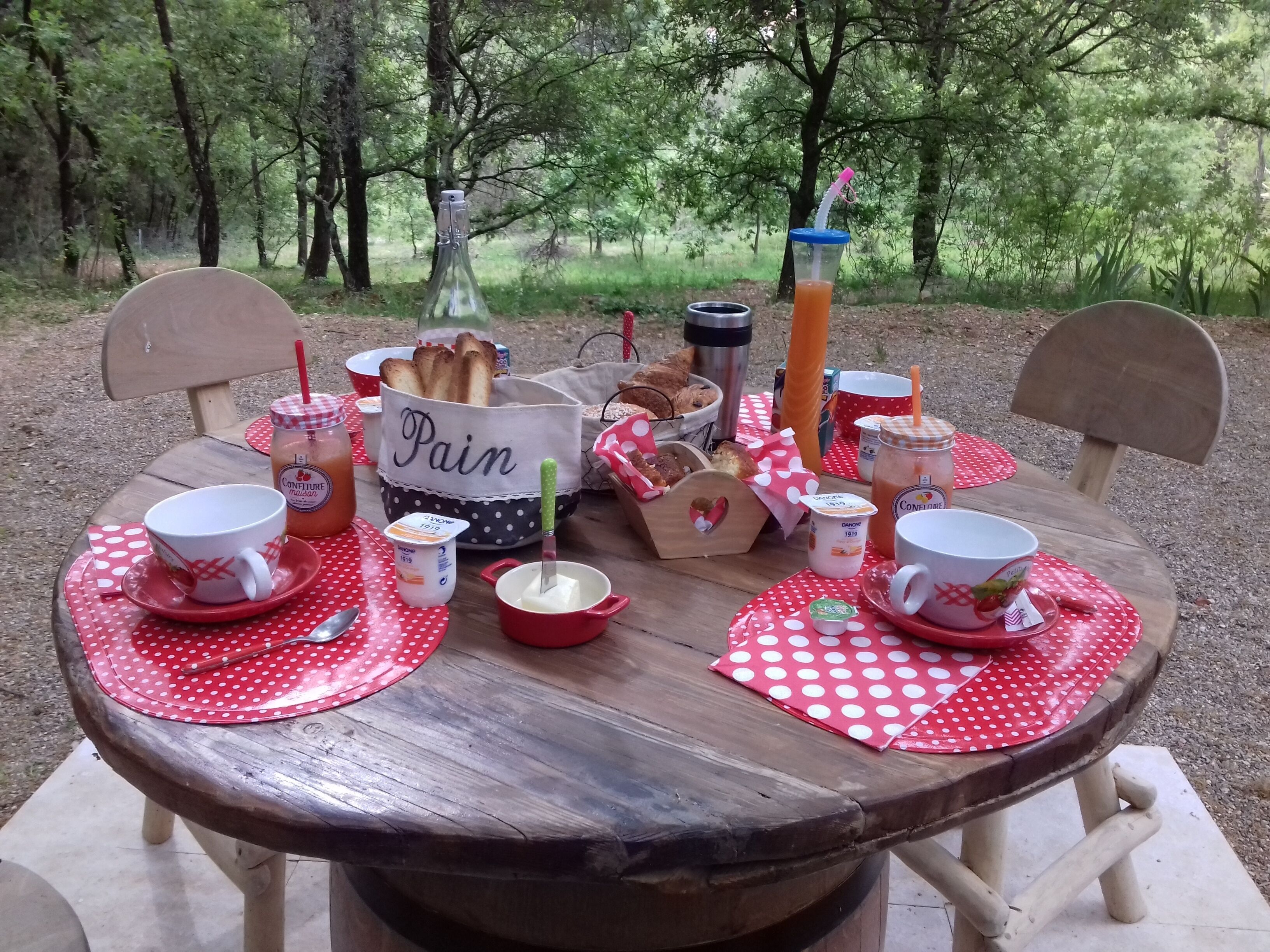 Montaje de picnic con una mesa de madera, individuales de lunares rojos y diversos alimentos y bebidas.