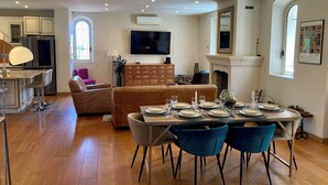 A dining area with a wooden table set for four, surrounded by blue chairs, a brown sofa, and a TV in the background.