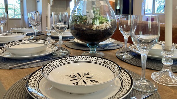 A dining table set with plates, glasses, and a decorative bowl with greenery.