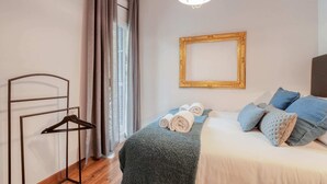 Une chambre d’hôtel avec un lit, un luminaire suspendu, un tableau encadré au mur et une fenêtre avec des rideaux.