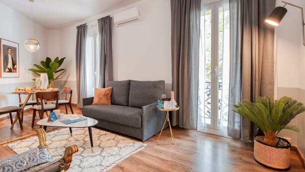 Un salon avec un canapé gris, une table basse, un coin repas avec des chaises, une plante et une lampe.