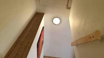 A narrow stairway with wooden steps and a handrail, leading to a landing with a small circular window.