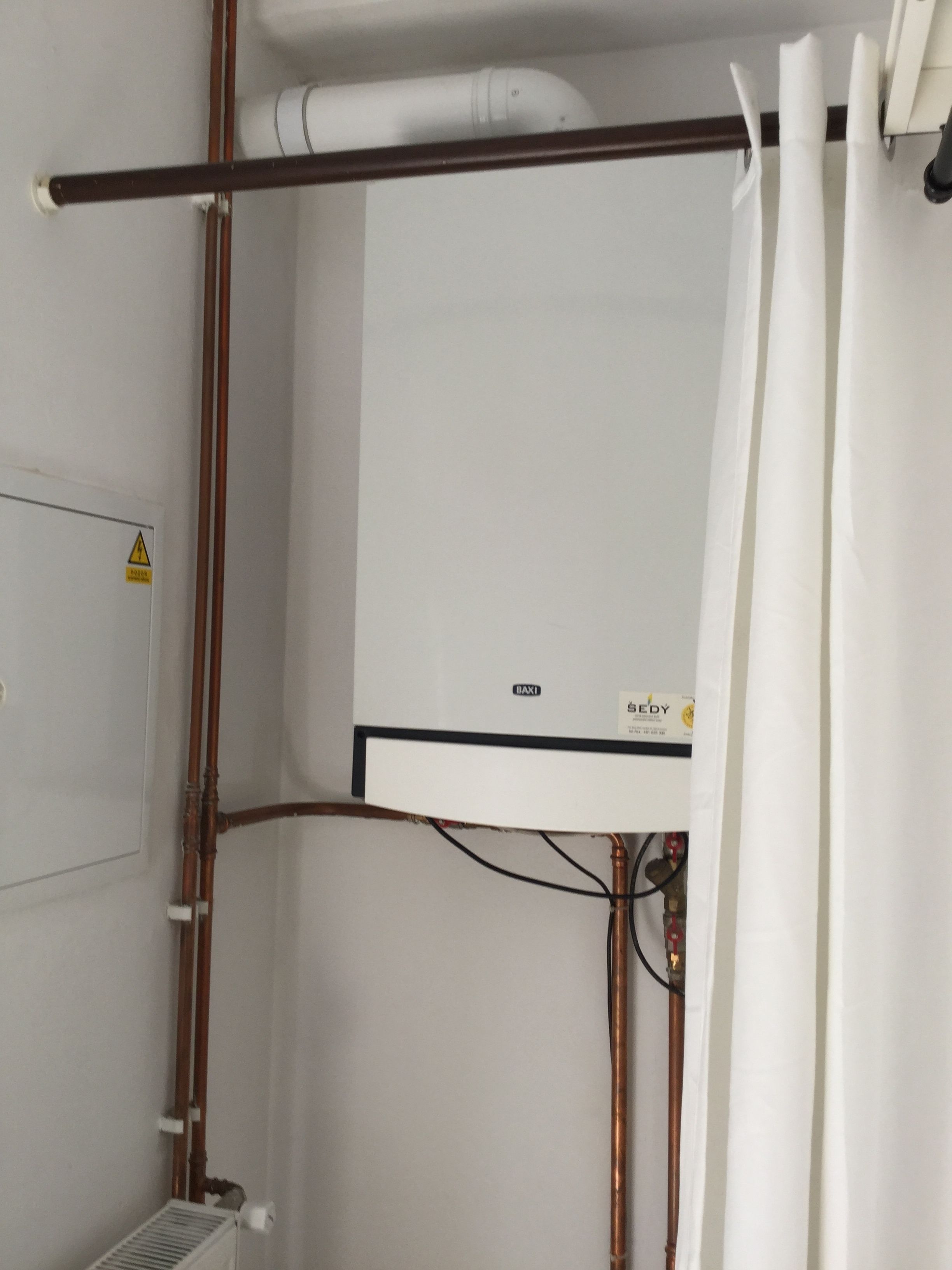 A bathroom with a white shower curtain, a visible water heater, and exposed plumbing.
