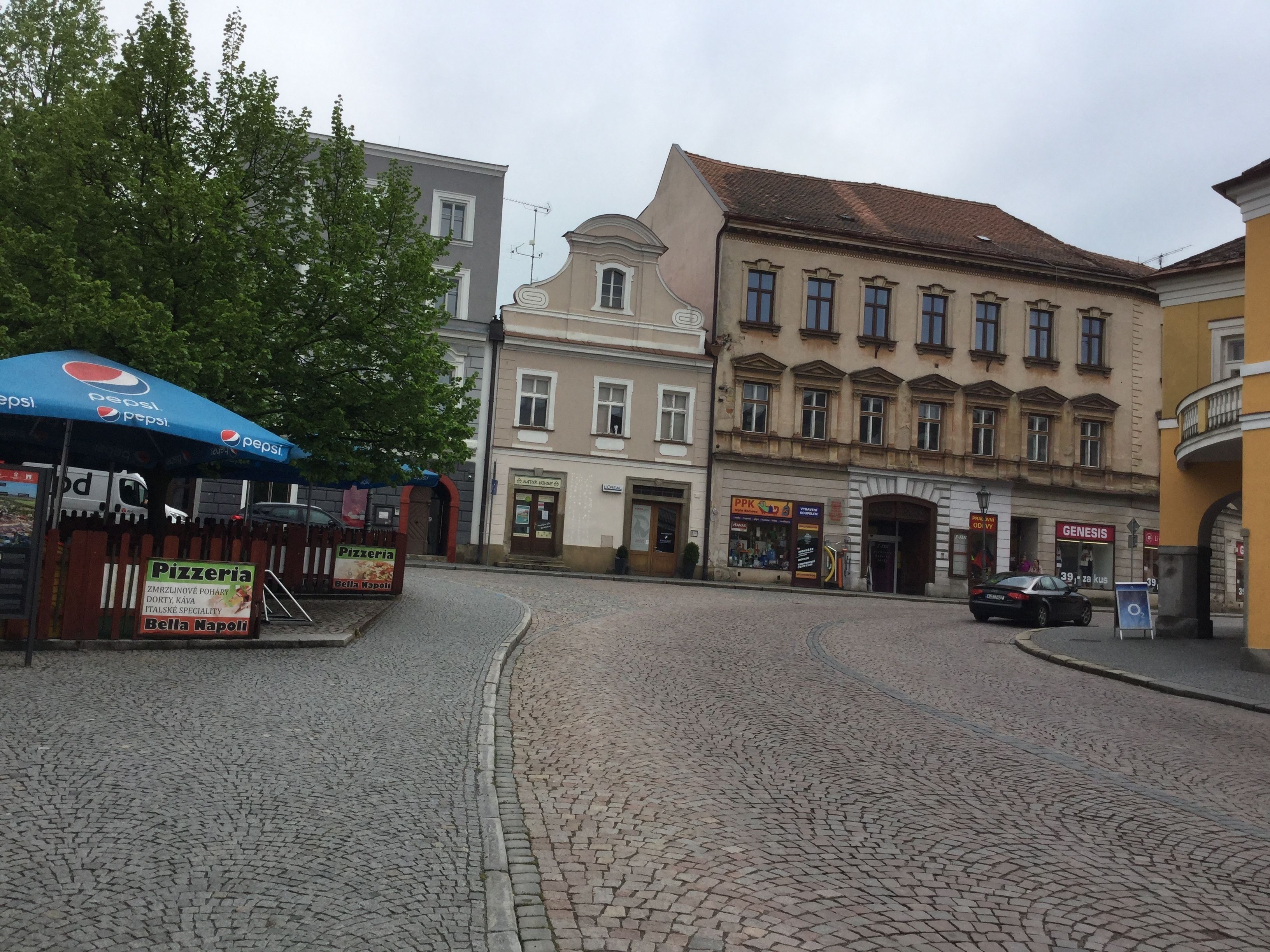 A cobblestone street with buildings, a pizzeria, and a car parked on the side.