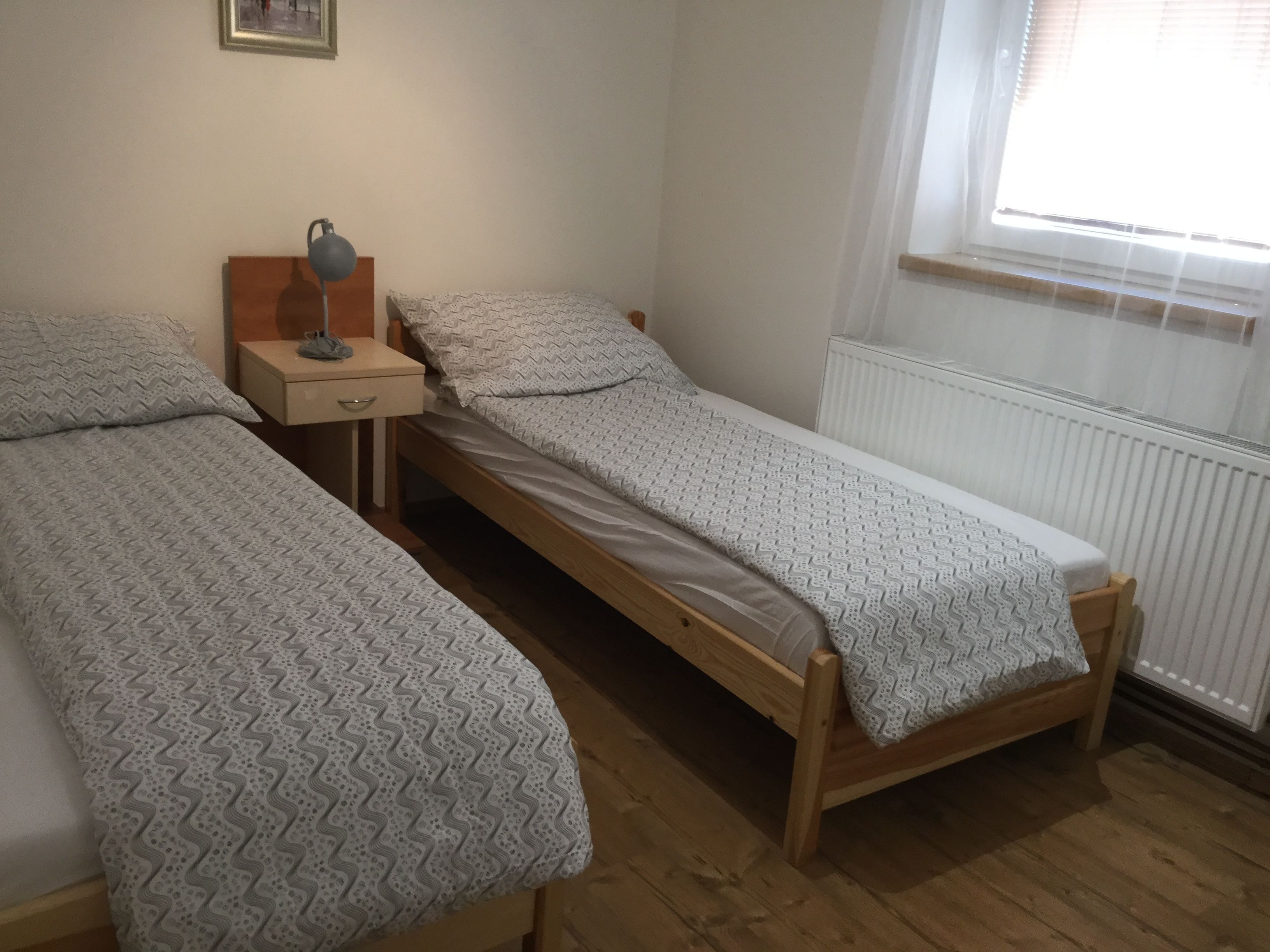 A bedroom with two single beds, a bedside table with a lamp, and a radiator.