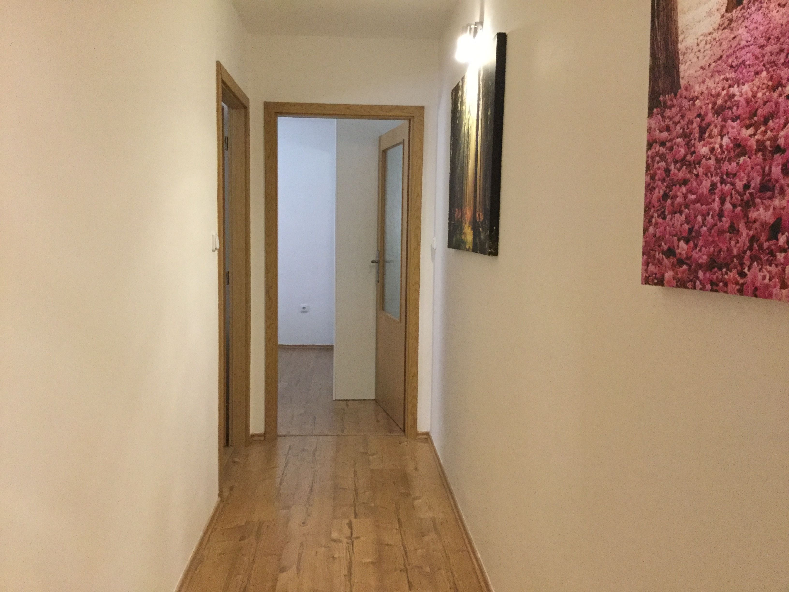 A narrow hallway with wooden flooring and white walls.
