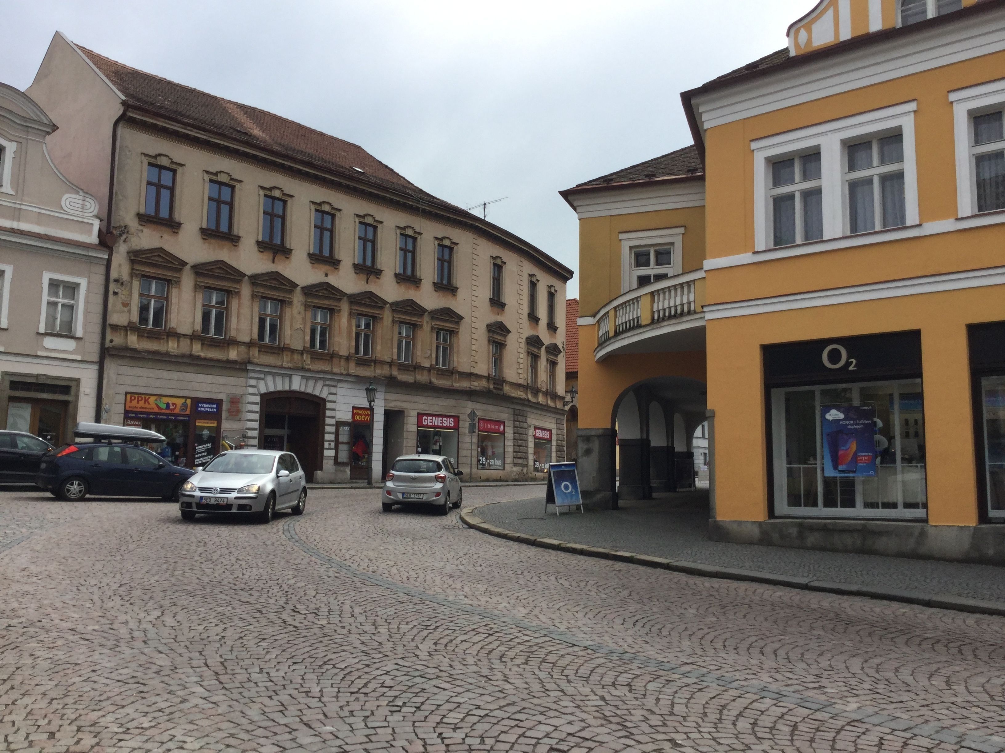 Eine Kopfsteinpflasterstraße mit historischen Gebäuden, ein am Straßenrand geparktes Auto und ein Laden mit dem Schild "GENESIS".