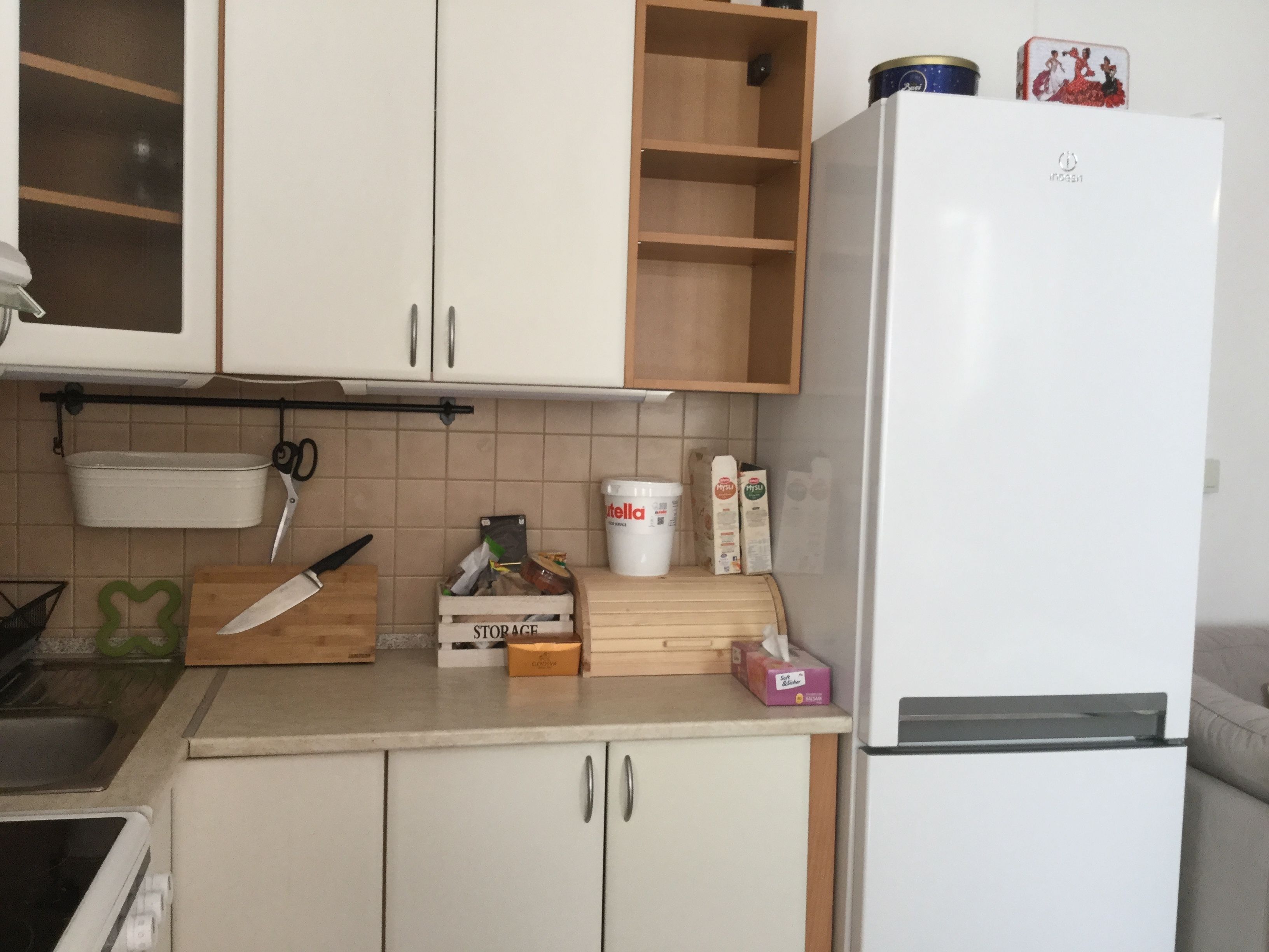 A kitchen with white cabinets, a wooden countertop, a white refrigerator, and a small wooden shelf with decorative items.