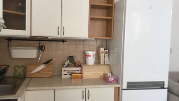A kitchen with white cabinets, a wooden countertop, a white refrigerator, and a small wooden shelf with decorative items.