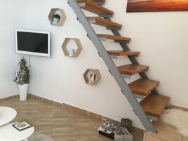 Una escalera moderna con escalones de madera y barandillas metálicas, un televisor de pantalla plana montado en la pared y estantes hexagonales decorativos.