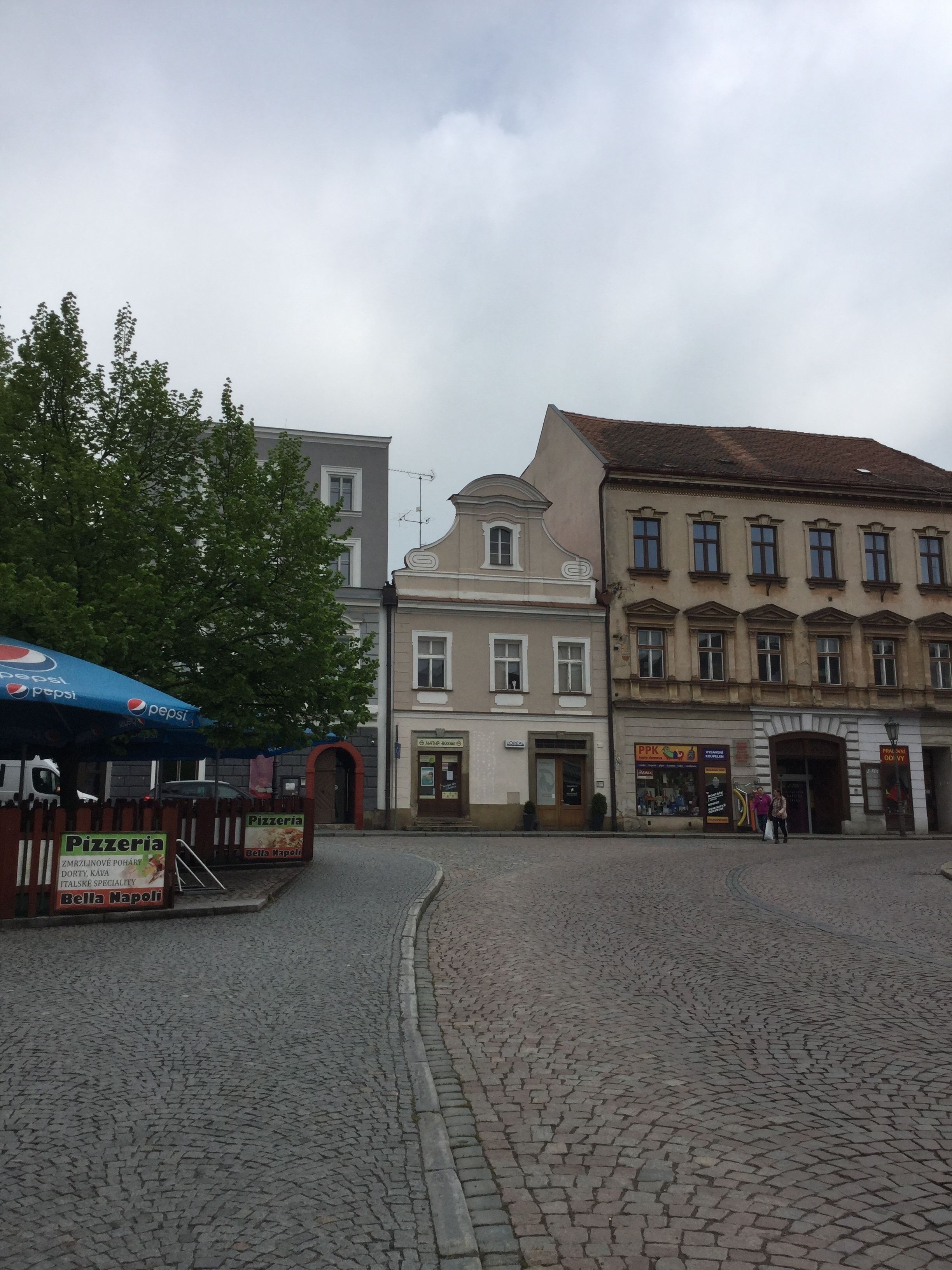 A cobblestone square with historic buildings, a pizzeria sign, and a Pepsi tent.