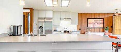 A modern kitchen with a central island, stainless steel appliances, and bright pendant lighting.