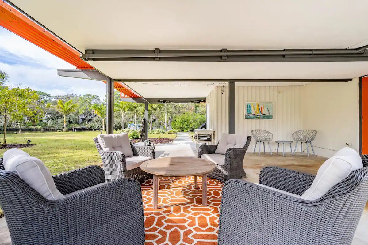 An outdoor patio with wicker furniture, a wooden table, and a patterned rug.