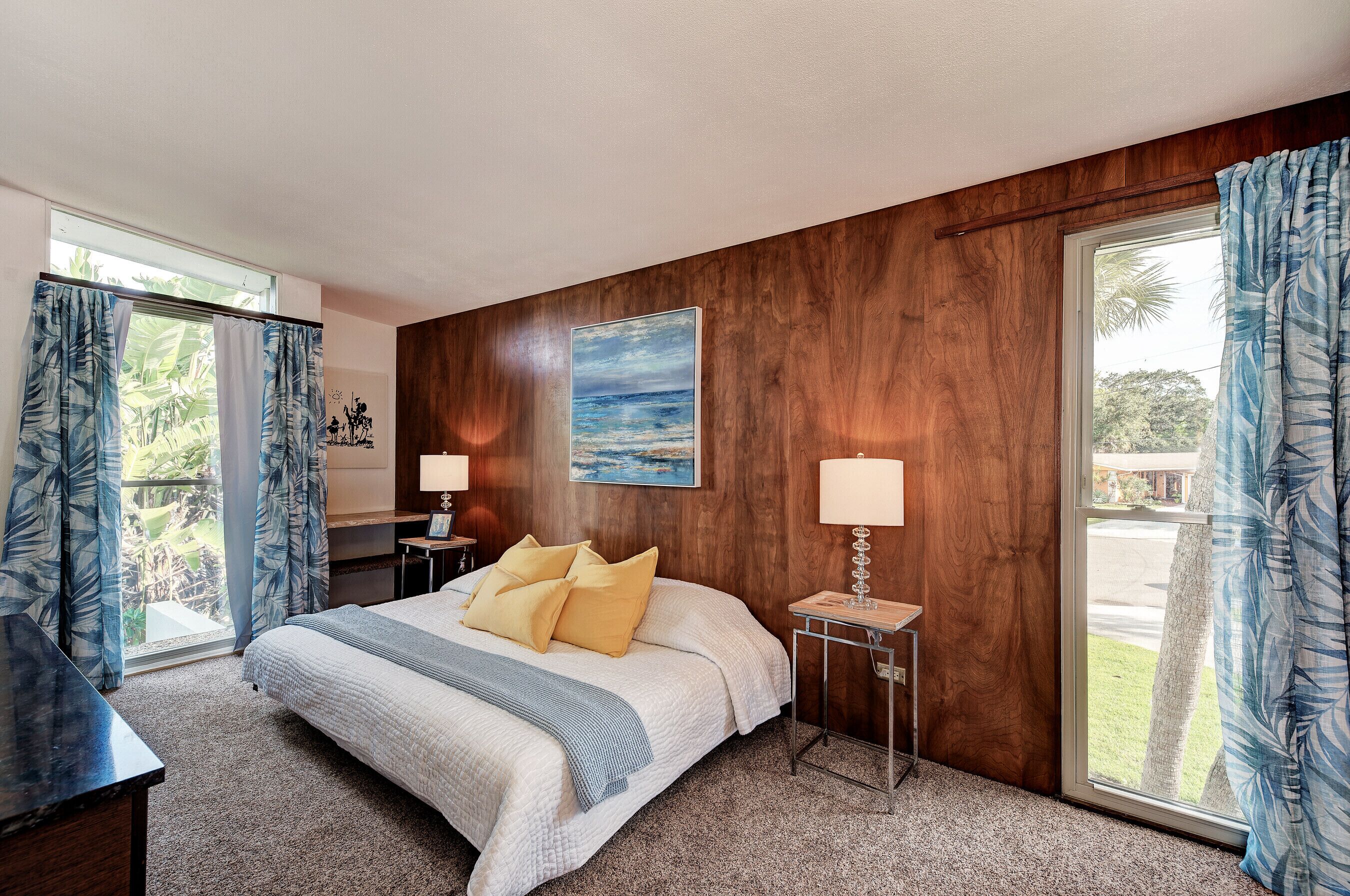 Une chambre à coucher avec un grand lit, deux tables de chevet avec des lampes, une fenêtre avec des rideaux et un tableau au mur.