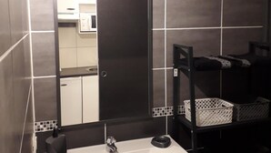Een badkamer met een witte wastafel, donkere tegels, een spiegel en een plank met manden.