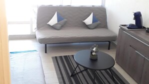 Een compacte leefruimte met een grijze bank, een kleine ronde tafel en een gestreept vloerkleed.
