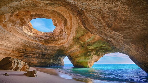 A natural rock formation with a circular opening, a sandy beach, and the ocean.