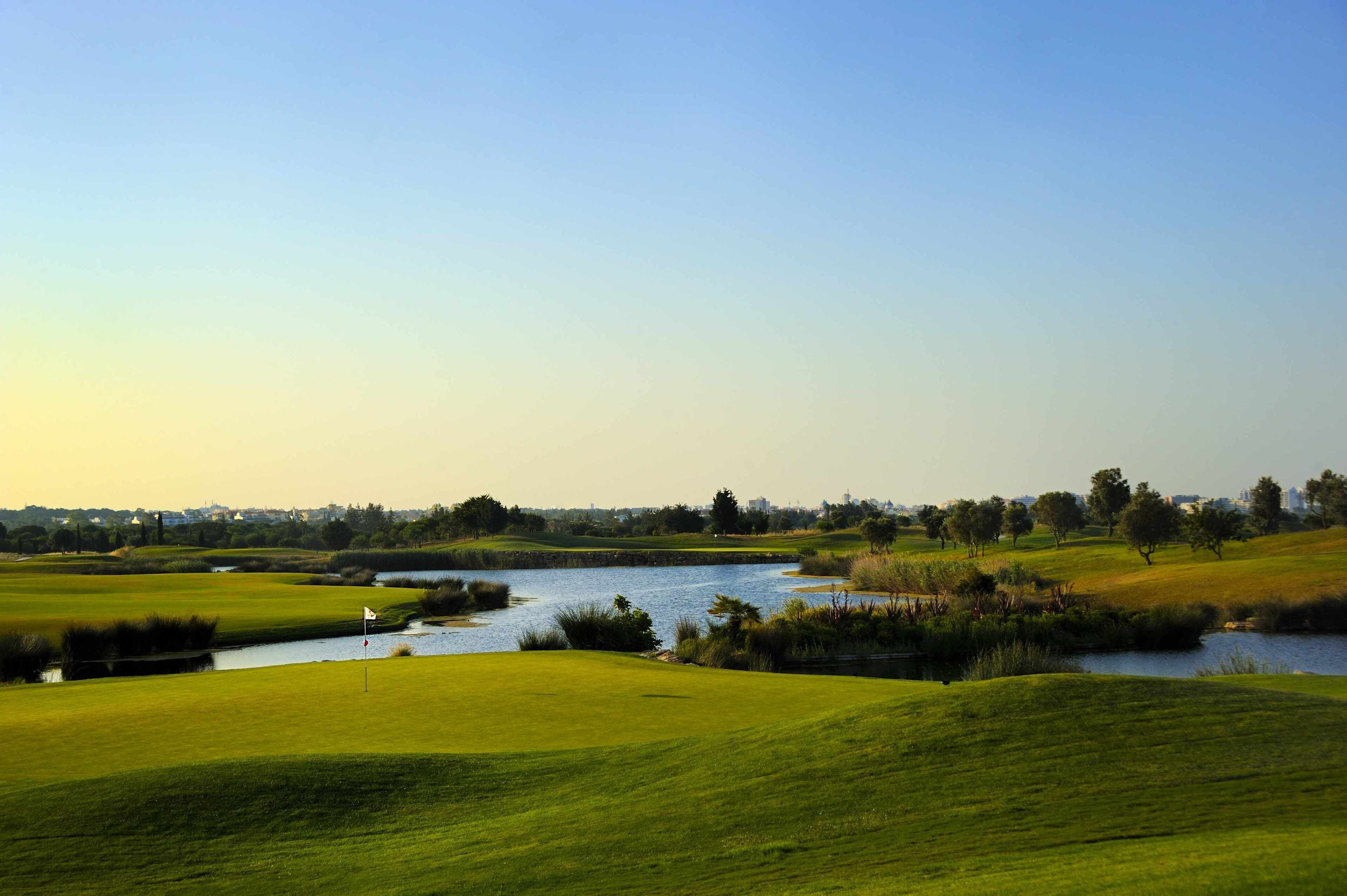 Un campo de golf con un cuerpo de agua, césped verde y árboles.