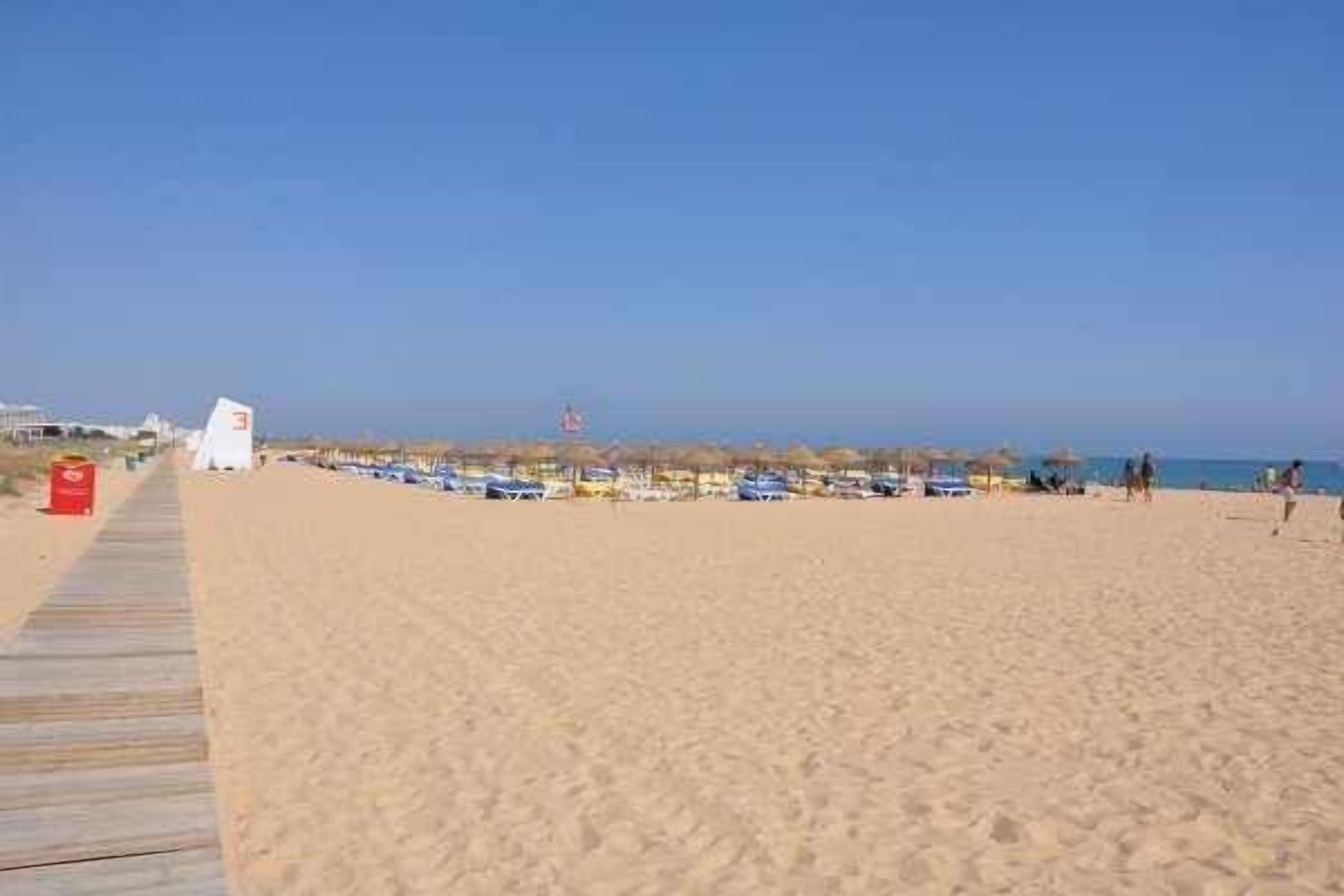 A sandy beach with a wooden boardwalk, beach umbrellas, and a lifeguard tower.