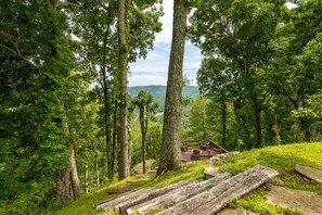 A wooden deck with seating, surrounded by dense forest and a distant view of hills.