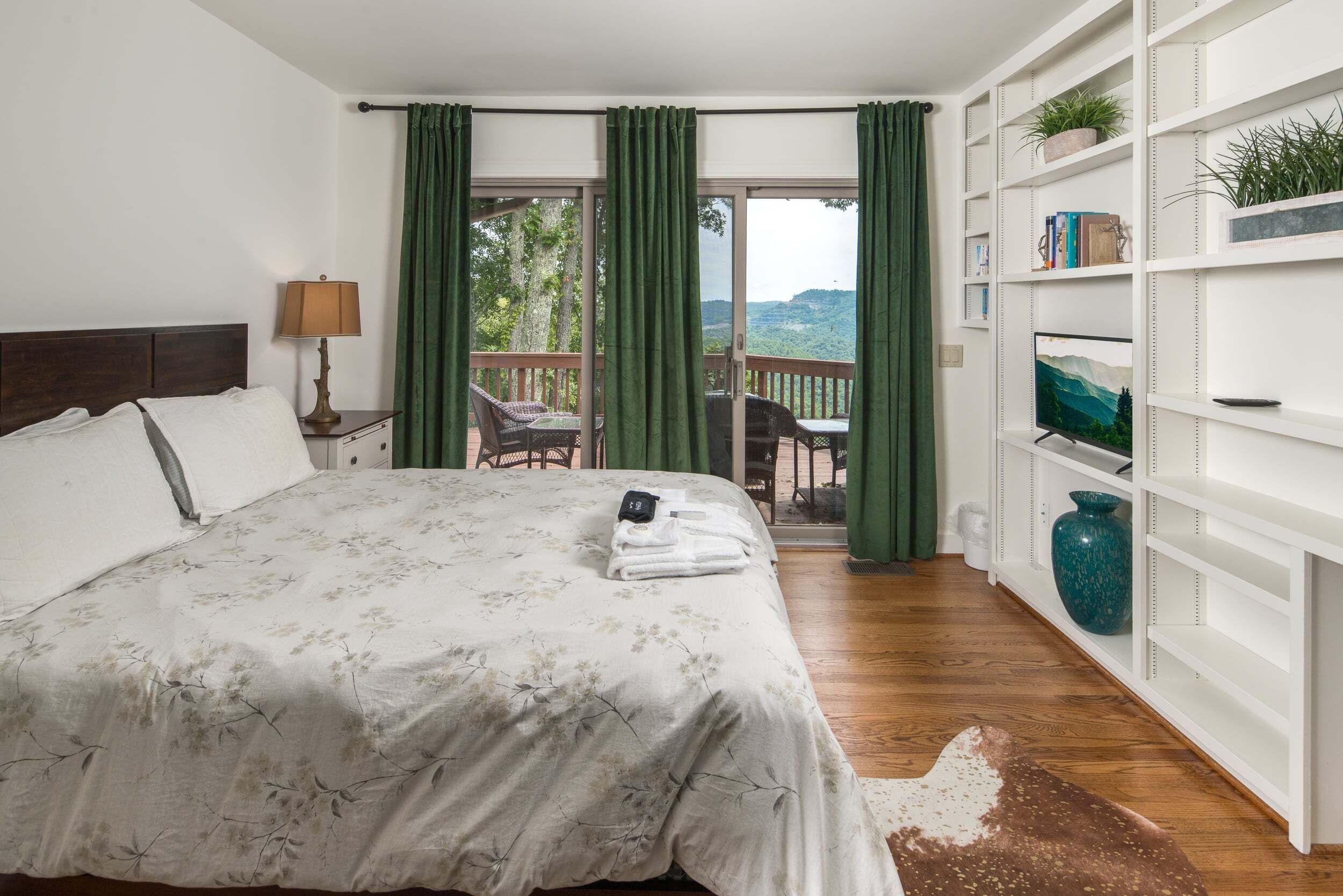 Une chambre à coucher avec un grand lit, une table de chevet, une lampe, une vue sur l’extérieur par une fenêtre et une bibliothèque.