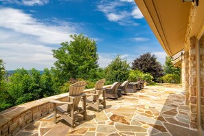 Un patio al aire libre con suelo de piedra, sillas de madera y vistas del paisaje circundante.