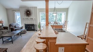 A modern kitchen with a central island, wooden stools, and a dining area with chairs. - Harbor Cove #39 | Private Beach Access on Little Traverse | Pool | Fireplace (Harbor Springs)