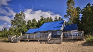 A beachside building with a blue roof, wooden deck, and a staircase leading to the entrance. - Harbor Cove #39 | Private Beach Access on Little Traverse | Pool | Fireplace (Harbor Springs)