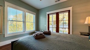 A bedroom with a large bed, two windows, and a view of the outdoors.