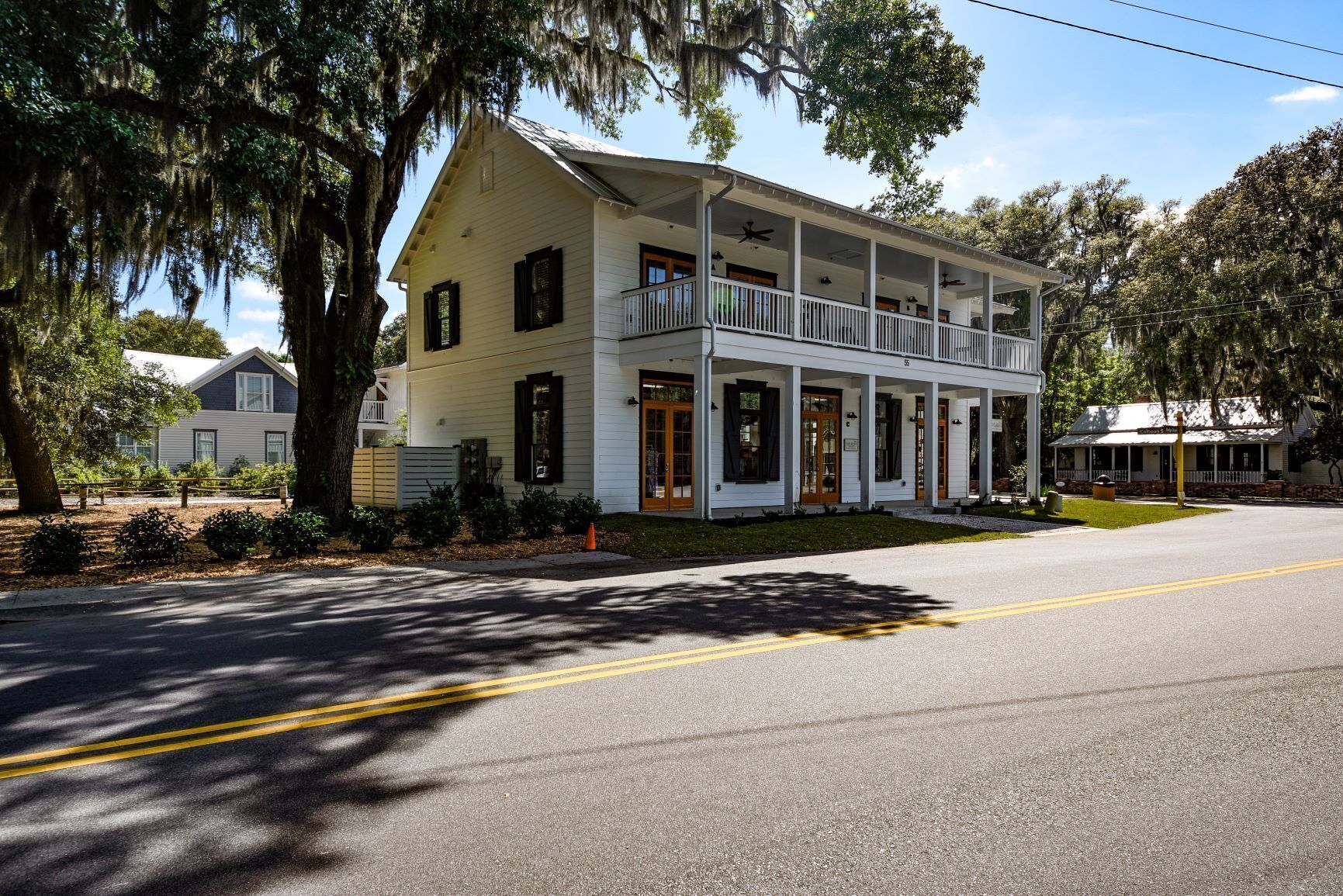 A two-story white building with a balcony, a porch, and a small garden area.