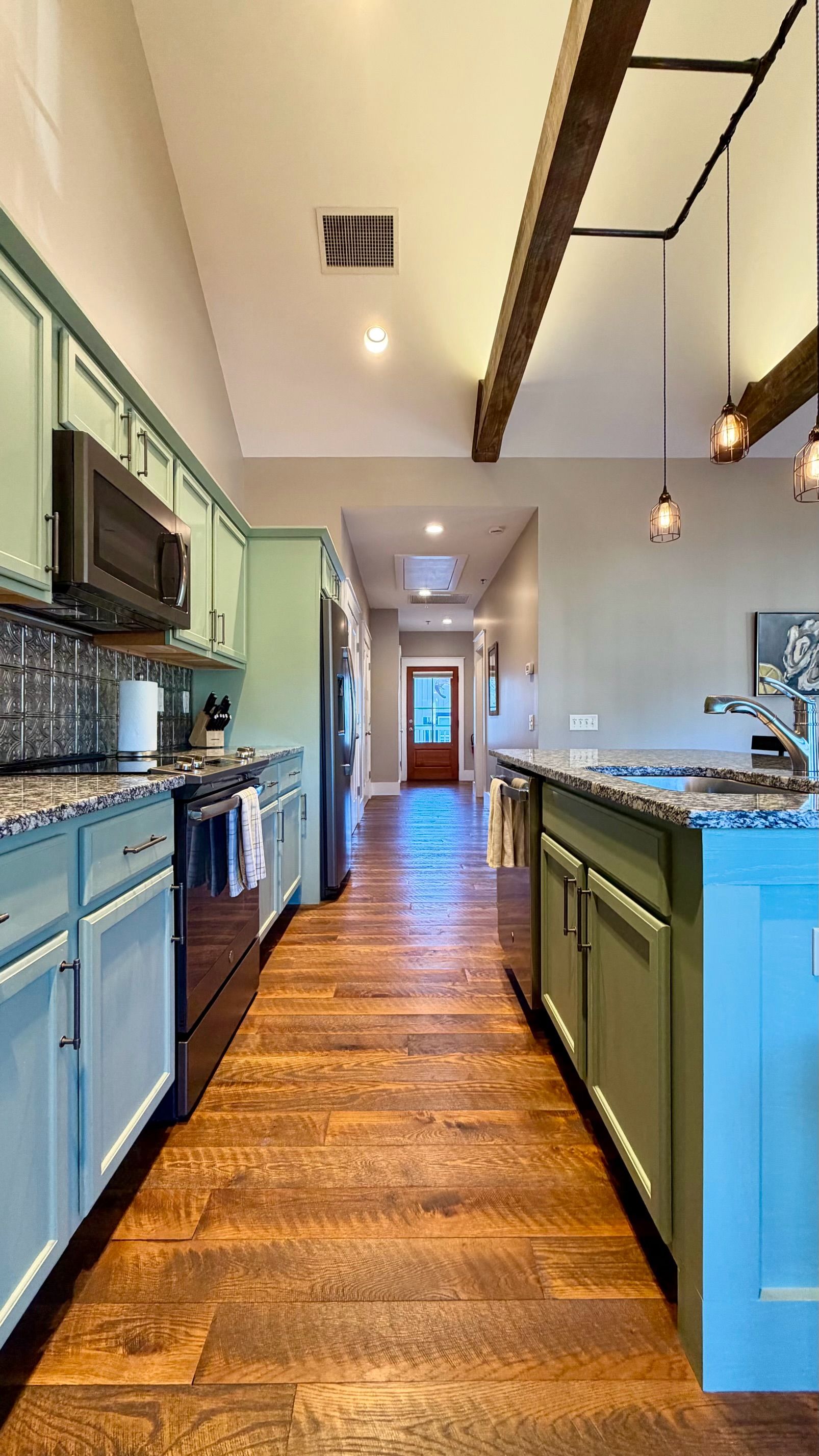 Una cocina con piso de madera, gabinetes verdes y un refrigerador de acero inoxidable.