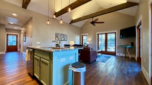 Una cocina amplia con una isla central, vigas de madera, iluminación colgante y un ventilador de techo.