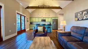 A spacious living room with a brown leather sofa, a wooden coffee table, and a dining area with a blue rug.