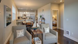 Un espacio habitable amplio con una mesa de comedor, dos sillones grises con almohadones con forma de estrella de mar, una pequeña mesa de centro de madera y un modelo decorativo de un velero.