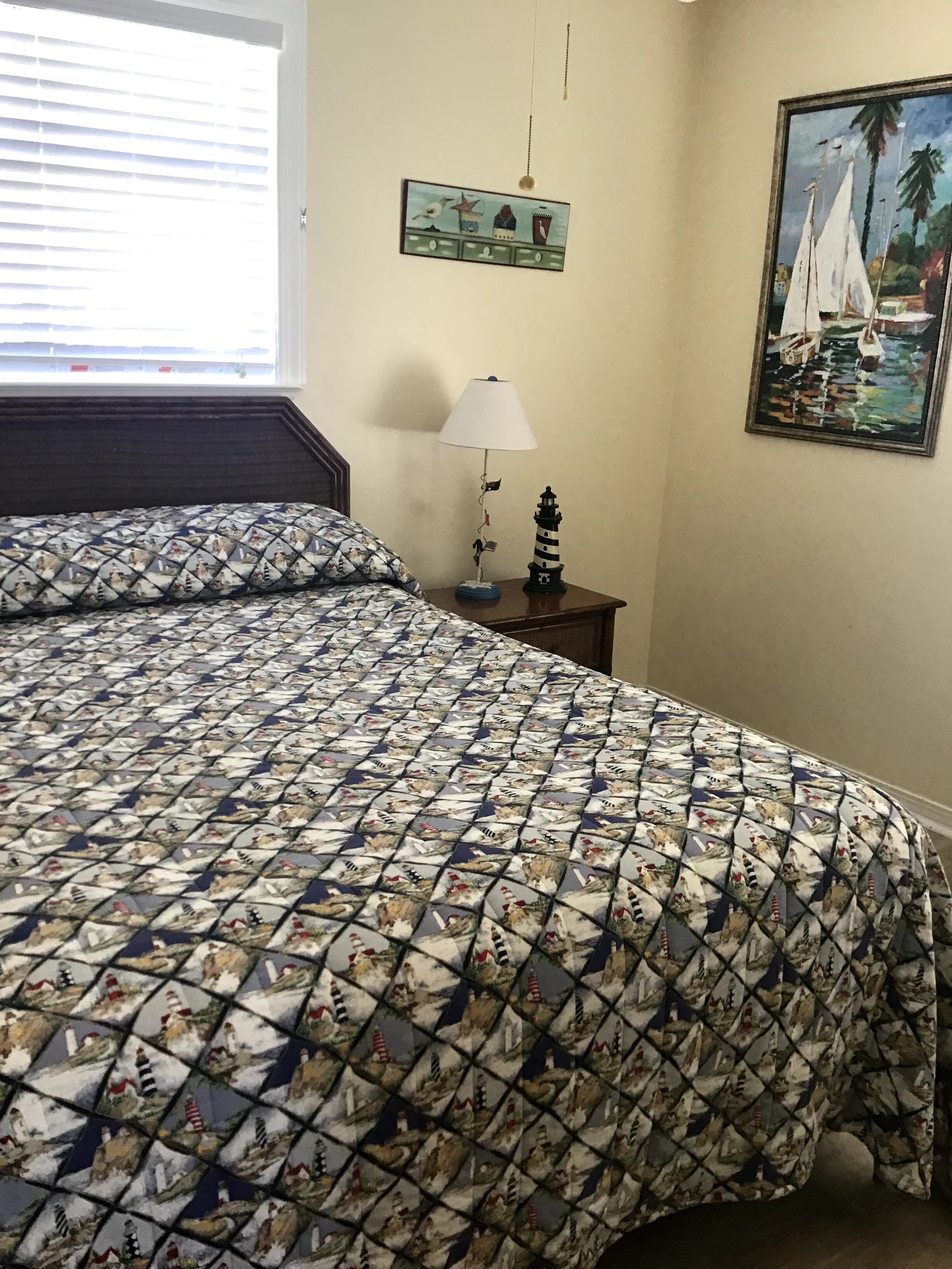 Una camera da letto con un letto ricoperto da una coperta a motivi decorativi, un comodino con una lampada, un quadro appeso al muro e una finestra con persiane.