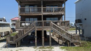 Un edificio de madera de varios pisos con un balcón en el nivel superior, ubicado en una playa arenosa bajo un cielo azul claro.