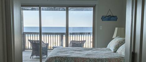 Een slaapkamer met een bed, een plafondventilator en uitzicht op het strand door een schuifdeur.